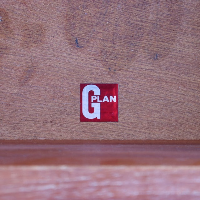 Close-up of vintage teak wood panel with G-Plan British mid-century furniture logo in red and white square label.
