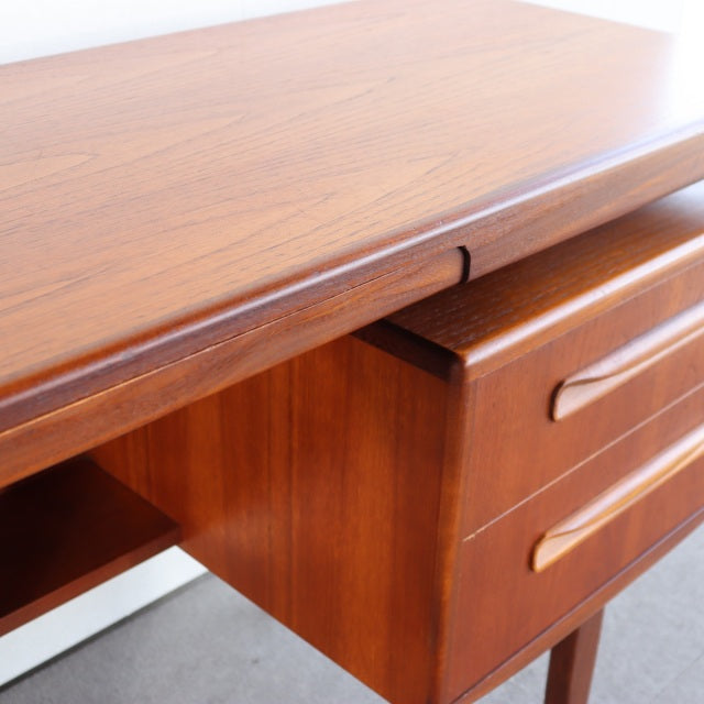 Vintage British mid-century teak desk with smooth wood grain, rounded edges, and integrated drawer pulls.