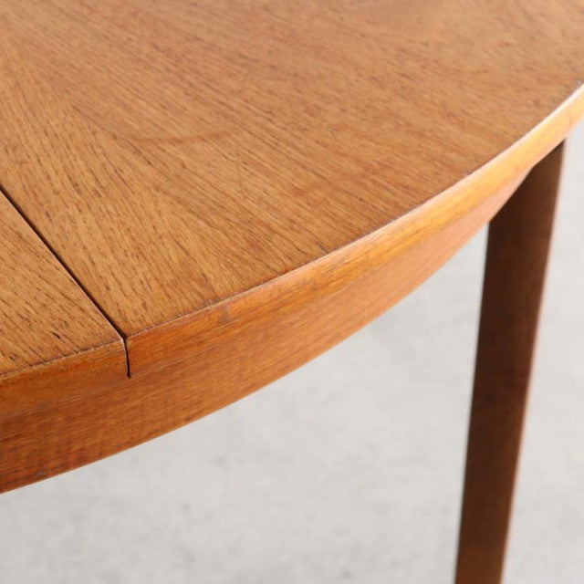 Close-up of vintage teak dining table corner with smooth rounded edge and slender tapered leg, showcasing mid-century.