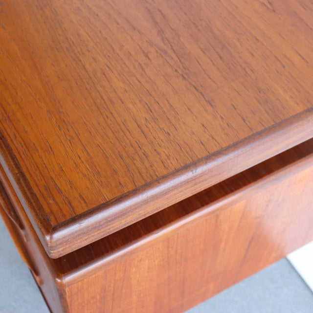 Close-up of vintage British mid-century teak desk corner with smooth wood grain and rounded edge detail.