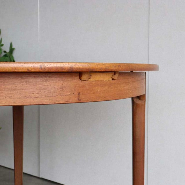 Mid-century British vintage teak dining table with rounded edge, slender tapered legs, and visible wood grain.