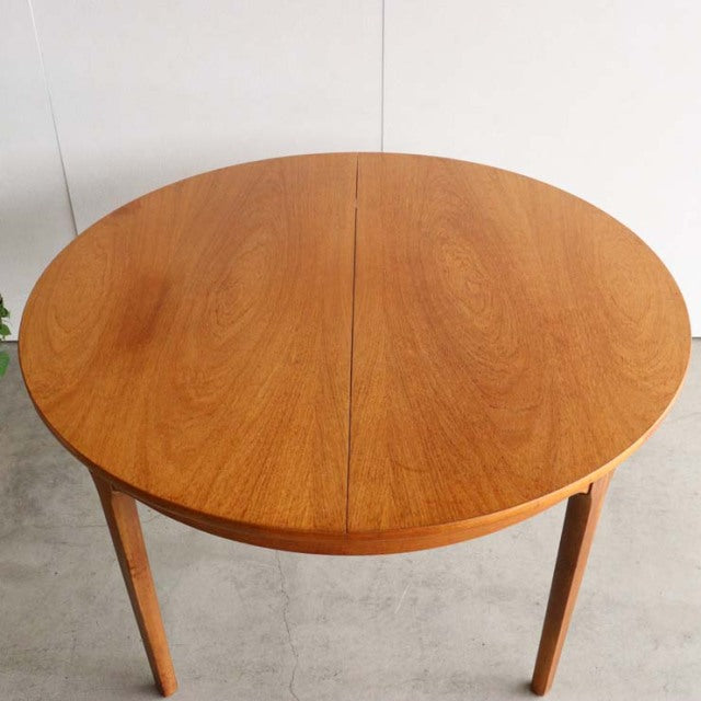 Round vintage teak dining table with visible wood grain, slender tapered legs, mid-century British design inspired by.