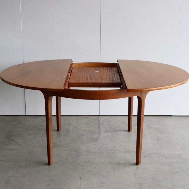 Mid-century British vintage teak dining table with oval top, extending mechanism, and tapered legs.