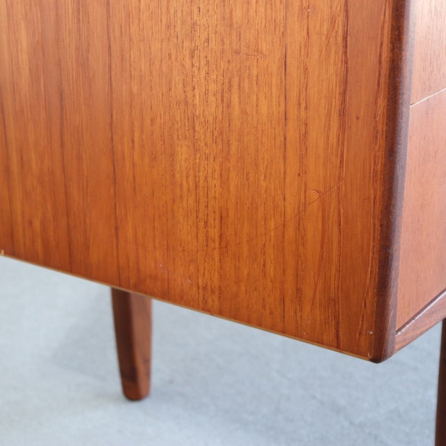 Close-up of vintage teak desk corner showcasing warm wood grain, sharp edges, and tapered British mid-century legs.