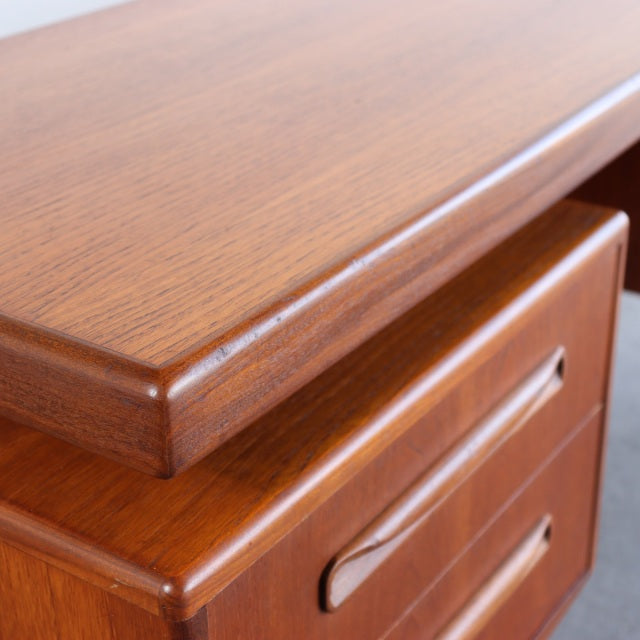 Close-up of vintage teak G-PLAN desk corner showing smooth wood grain, rounded edges, and integrated drawer handles in.