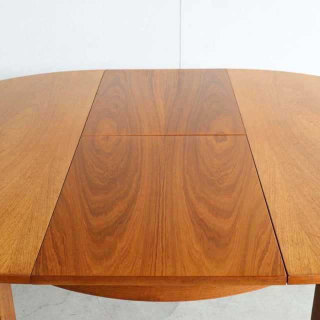 Mid-century British vintage teak dining table with oval top and visible wood grain pattern.