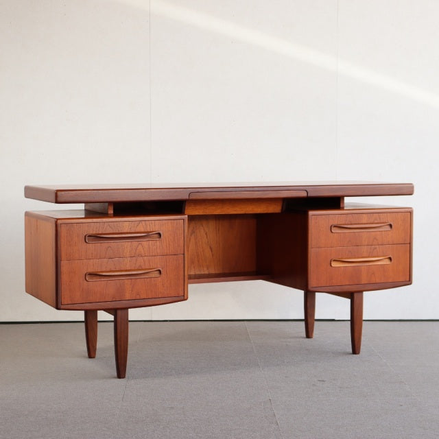Mid-century vintage teak desk by British G-PLAN, rich wood grain, four drawers, tapered legs, sleek rectangular form.