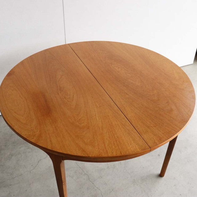Vintage British mid-century teak dining table with round top and tapered legs, smooth wood grain finish.
