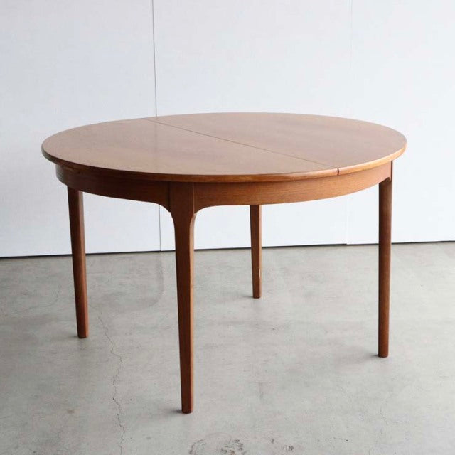 Vintage mid-century British teak dining table with round top and tapered legs, smooth wood grain finish.