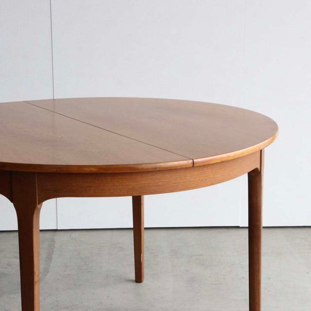 Vintage teak dining table with smooth round top, slender tapered legs, mid-century British-Denmark design.