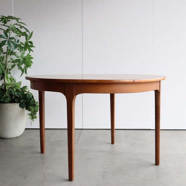 Mid-century British vintage teak dining table with oval top, smooth wood grain, and slender tapered legs.