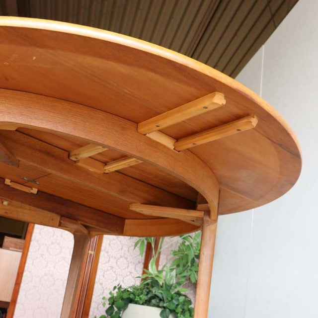 Mid-century British vintage teak dining table with round top, visible wood grain and sturdy wooden supports underneath.
