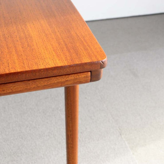 Mid-century British McIntosh teak coffee table corner with visible wood grain and tapered round leg.