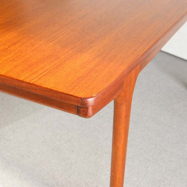 Vintage British mid-century teak coffee table corner with smooth rounded edges and tapered legs showing rich wood grain.
