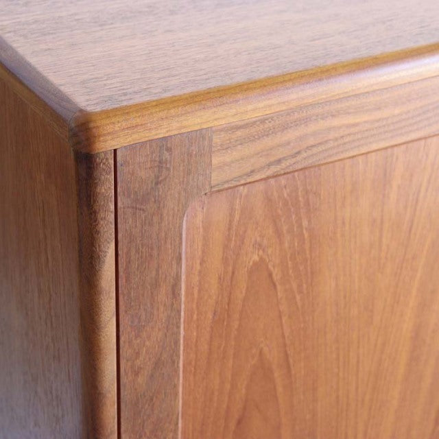 Close-up of vintage British mid-century teak sideboard corner showing smooth wood grain and rounded edge craftsmanship.