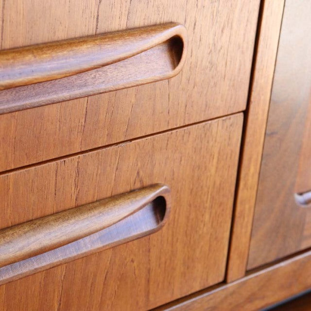 Close-up of vintage British mid-century teak sideboard drawers with carved recessed handles and rich wood grain.
