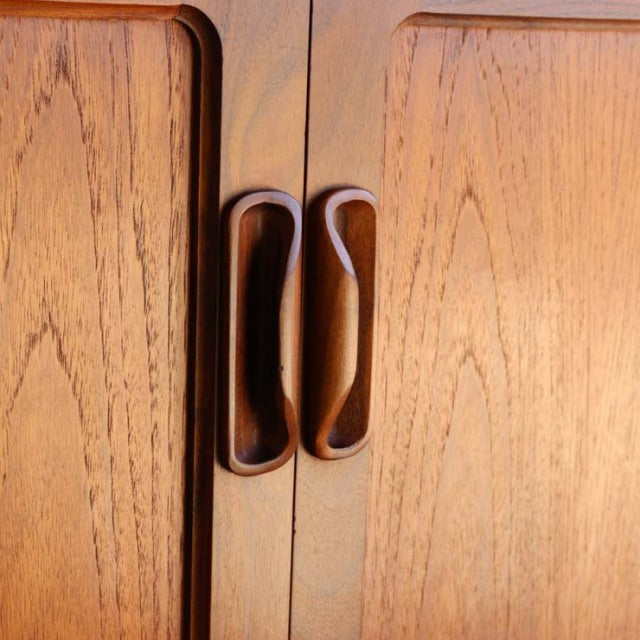 Close-up of vintage British mid-century G-PLAN Fresco teak sideboard showing curved recessed wooden handles and warm wood.