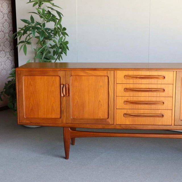 Vintage British G-Plan teak sideboard with rich wood grain, mid-century design, tapered legs, and rounded drawer handles.