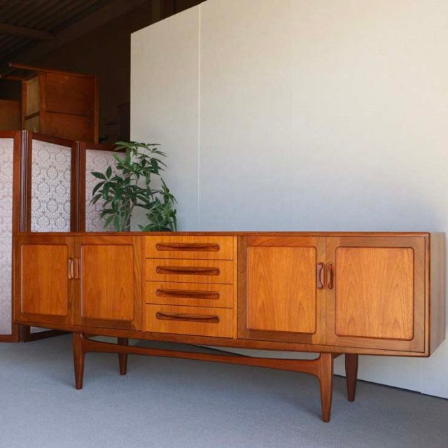 Vintage British mid-century teak sideboard by G-PLAN with rich wood grain, four drawers, two cabinet doors, and tapered legs .