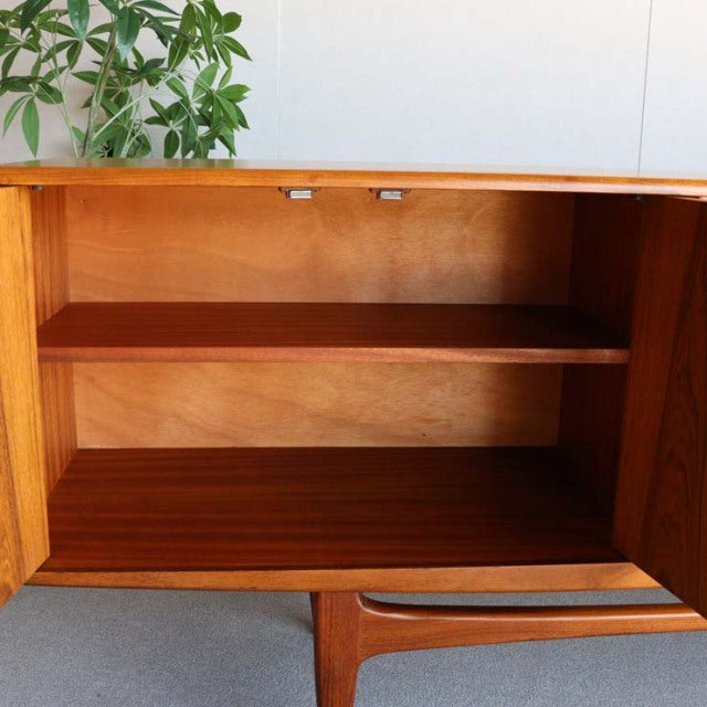 Mid-century British G-Plan Fresco teak sideboard with rich wood grain, open storage, and slender tapered legs.