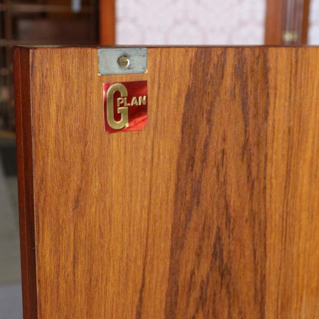 Close-up of vintage British G-PLAN teak wood sideboard door showing rich grain and original metal and red brand label.