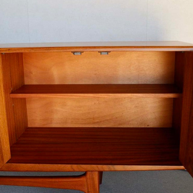 Mid-century British G-PLAN teak sideboard open cabinet showing warm wood grain and slender legs.