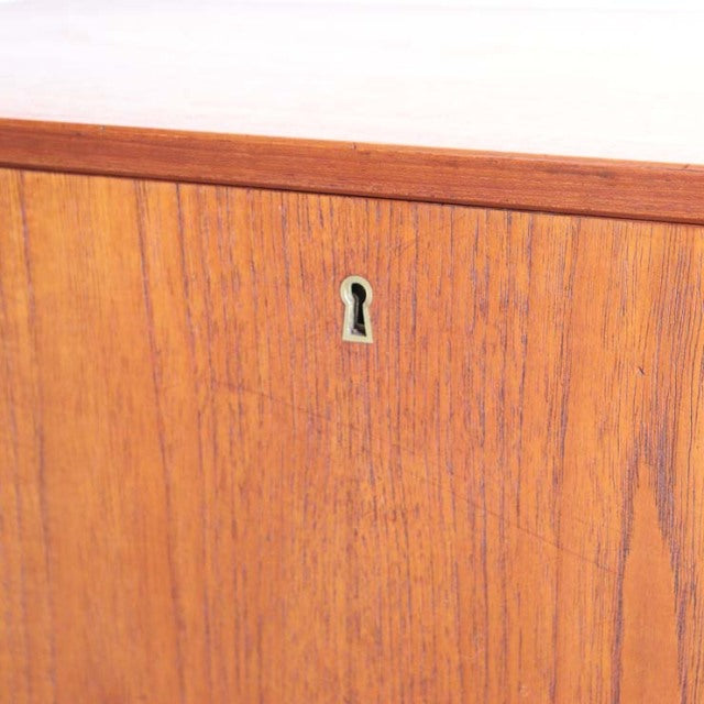 Close-up of vintage mid-century Danish teak cabinet door showing rich wood grain and small keyhole detail.