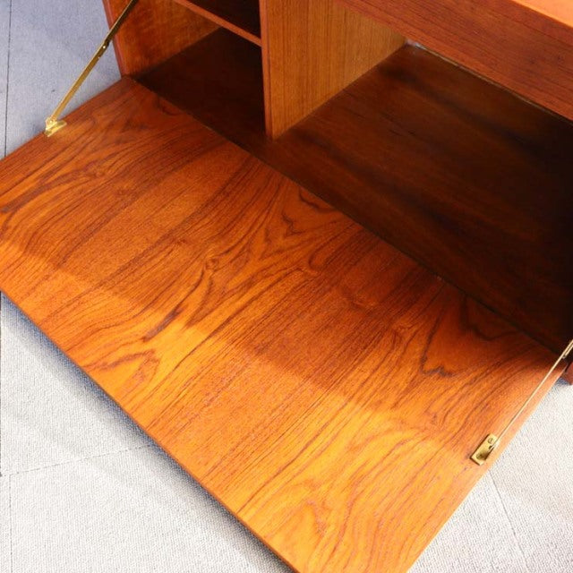 Mid-century Danish teak cabinet door open, showcasing rich wood grain and brass hinge details.