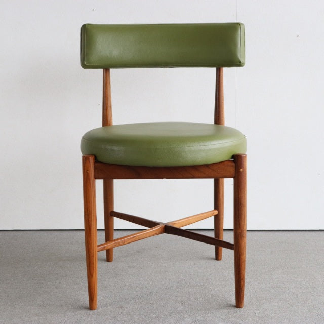 Vintage British mid-century teak dining chair with round green leather seat and backrest, sleek tapered legs, and cross.