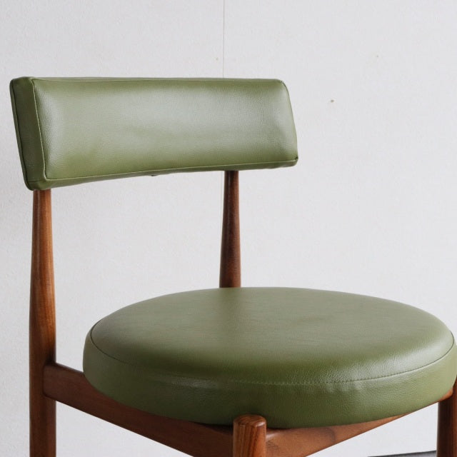 Vintage mid-century British teak dining chair with round olive green leather seat and matching backrest, elegant wood grain.