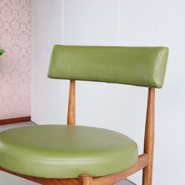 Vintage mid-century British teak dining chair with round olive green vinyl seat and backrest, slender tapered legs.