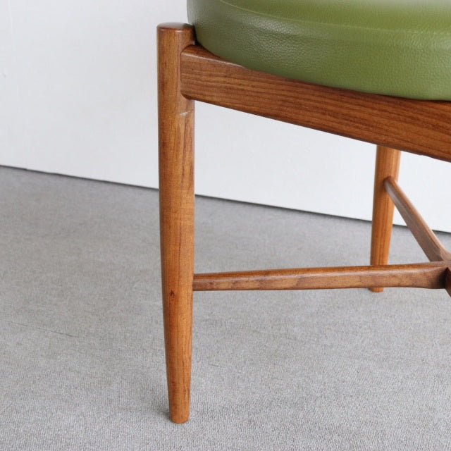 Mid-century British vintage teak dining chair leg with warm wood grain and olive green leather seat upholstery.