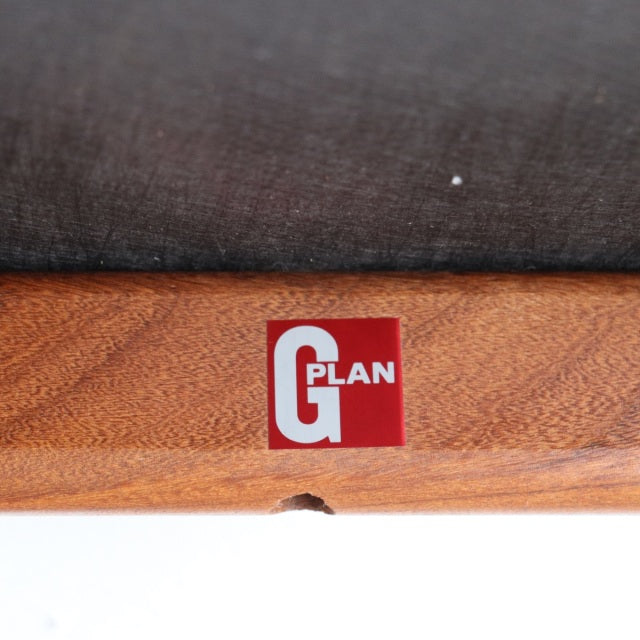 Close-up of vintage G-Plan teak chair frame with visible wood grain and dark upholstered seat, mid-century British design.