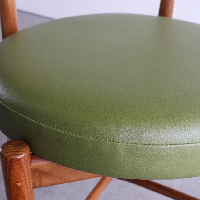 Vintage mid-century British teak dining chair with round olive green leather seat and visible wood grain legs.