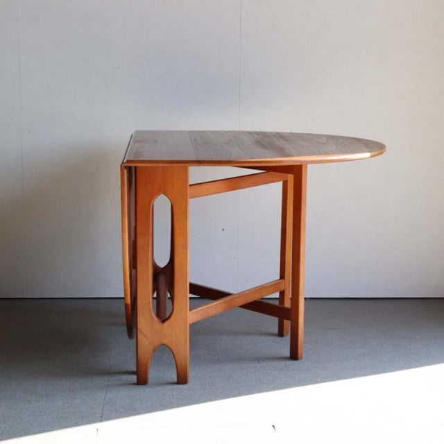 Mid-century British Jentique teak drop-leaf table with rounded top, visible wood grain, and slender tapered legs.