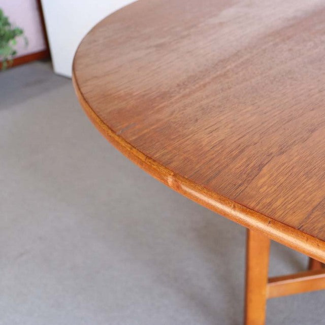 Round mid-century vintage teak drop-leaf table by British brand JENTIQUE, smooth wood grain visible on tabletop edge and.