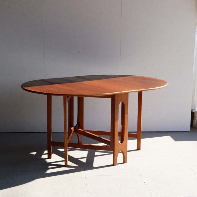 Mid-century British vintage teak drop-leaf table by Jentique with smooth wood grain and slender tapered legs against a plain .