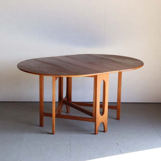 Vintage teak JENTIQUE mid-century British drop-leaf table with smooth oval top and slender tapered legs.