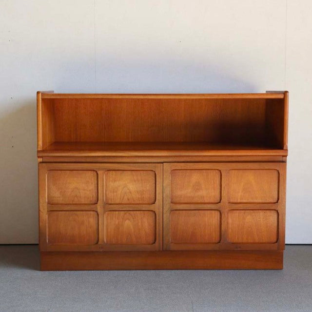 Mid-century British teak storage cabinet by Nathan with raised cross design on paneled doors, warm wood grain, and clean.