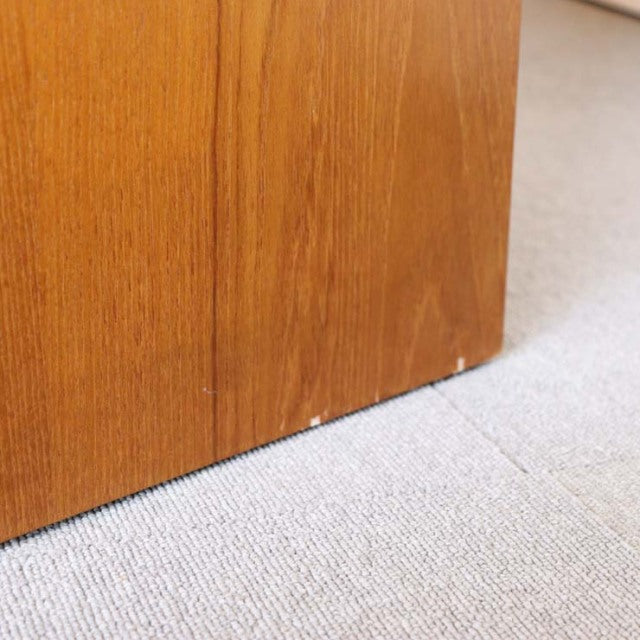 Close-up of vintage teak storage cabinet base showing smooth wood grain and subtle wear on corner, mid-century British.