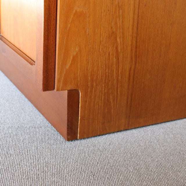 Close-up of mid-century British teak cabinet corner showing smooth wood grain and precise craftsmanship with recessed leg.