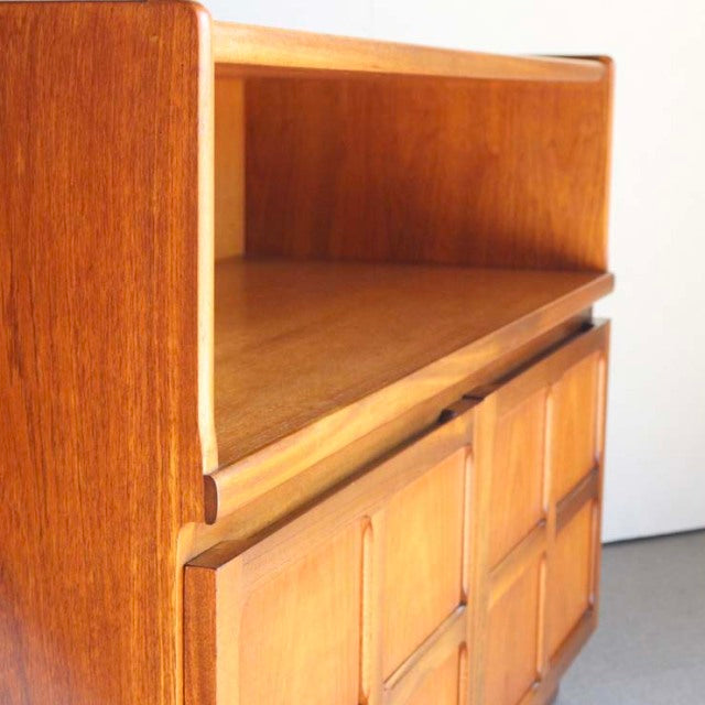 Mid-century British teak storage cabinet by Nathan with distinctive cross design on lower doors, smooth wood grain, and.