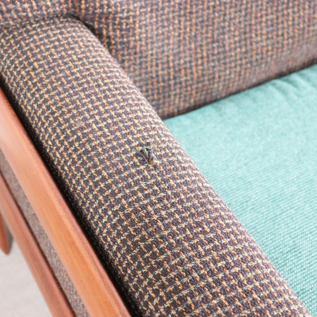 Close-up of vintage British mid-century teak sofa arm with textured Harris Tweed fabric showing a small wear spot, teal.