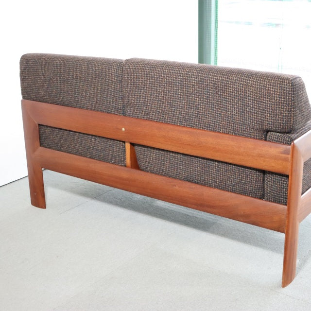 Vintage British mid-century teak two-seater sofa with clean lines, textured brown upholstery, and solid wood frame showing.