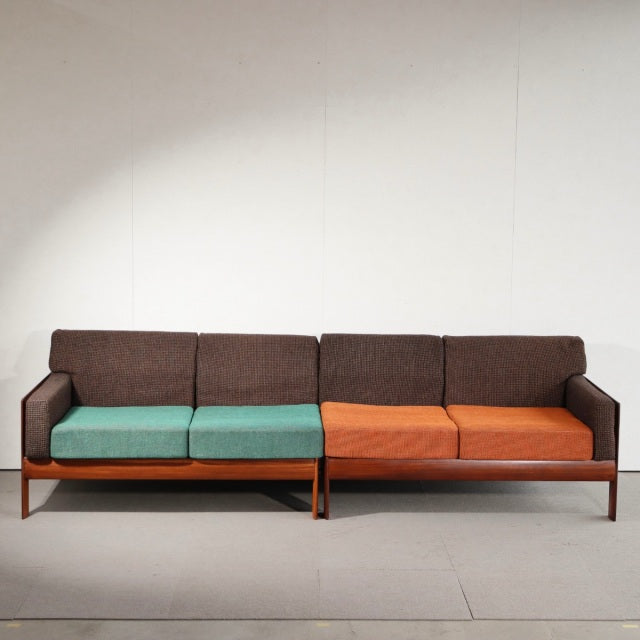 Vintage mid-century British teak two-seater sofa with clean lines, dark wood grain legs, and newly upholstered cushions in.