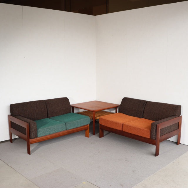Vintage mid-century British teak two-seater sofas with clean lines, dark wood grain frames, and reupholstered orange and.