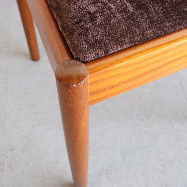 Close-up of vintage teak Meredew mid-century dining chair leg with smooth tapered wood grain and brown upholstered seat from .