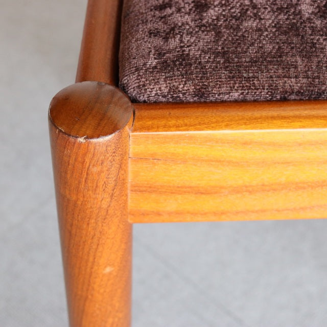 Close-up of mid-century British Meredew dining chair corner featuring warm teak wood grain and rounded leg detail with brown .