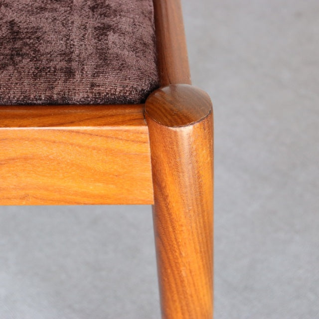 Mid-century British Meredew teak dining chair leg with rich wood grain and brown upholstered seat corner.