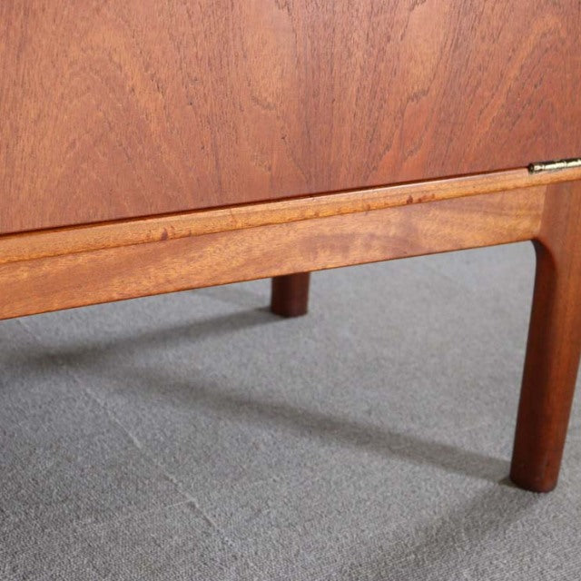 Mid-century British Macintosh teak cabinet leg with smooth wood grain and rounded edges on gray floor.